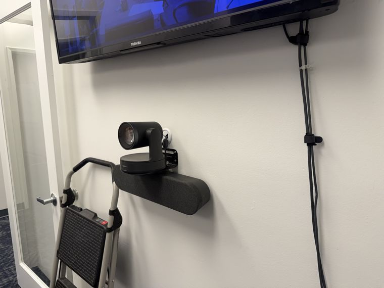 Meeting-room camera and speaker mounted below a wall display.