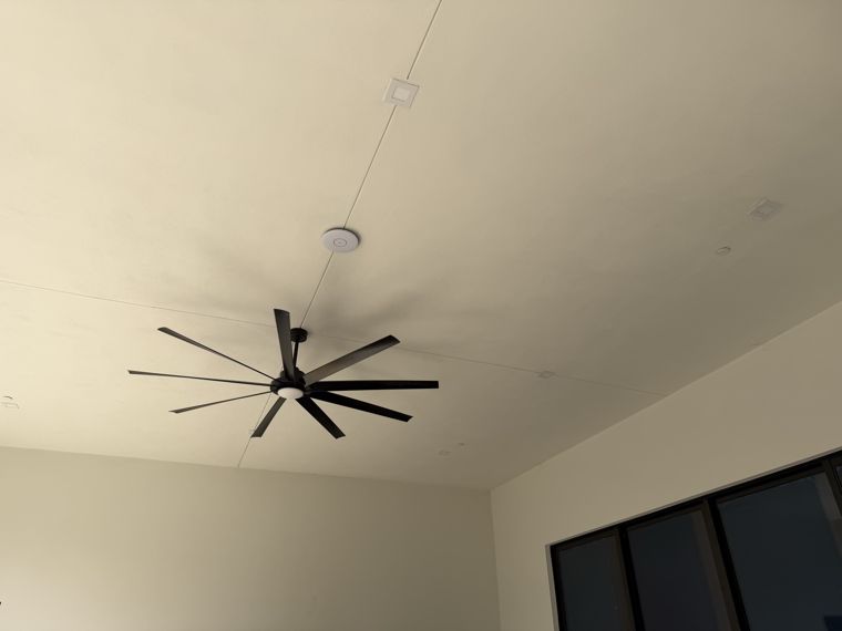 Ceiling-mounted wireless access point in a room with a ceiling fan.