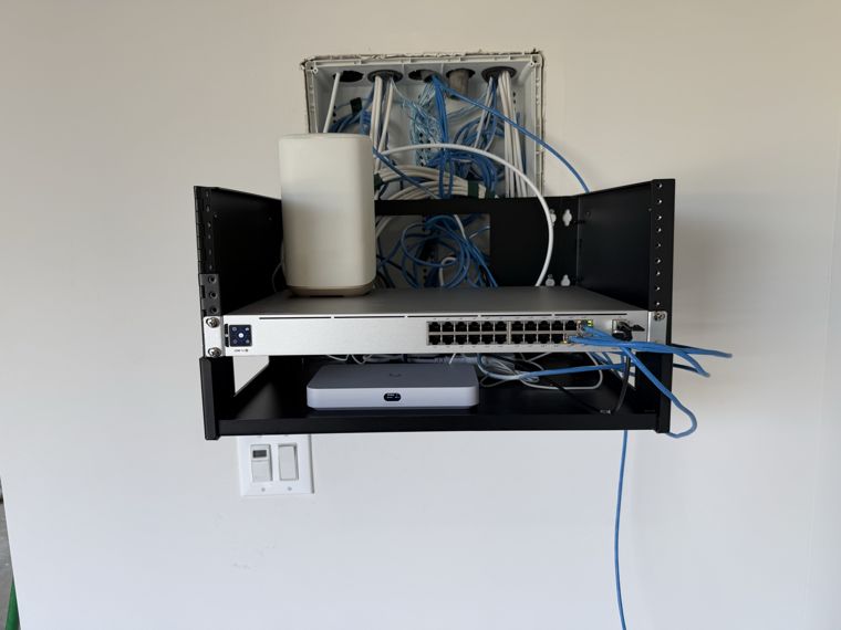 Wall-mounted network rack with a switch, gateway and blue Ethernet cabling.